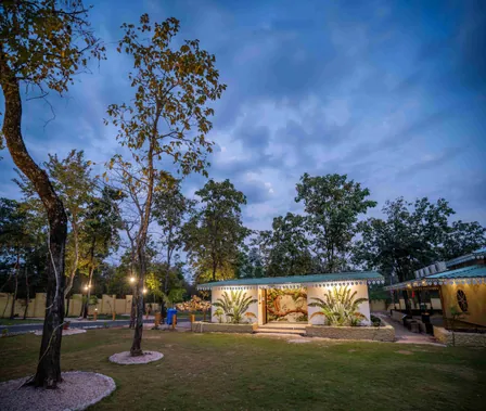 Cottages lit up at dusk under a blue sky at Palash Jungle Resort