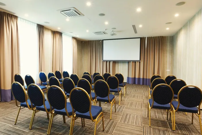 Conference hall set up with rows of chairs and a projector screen