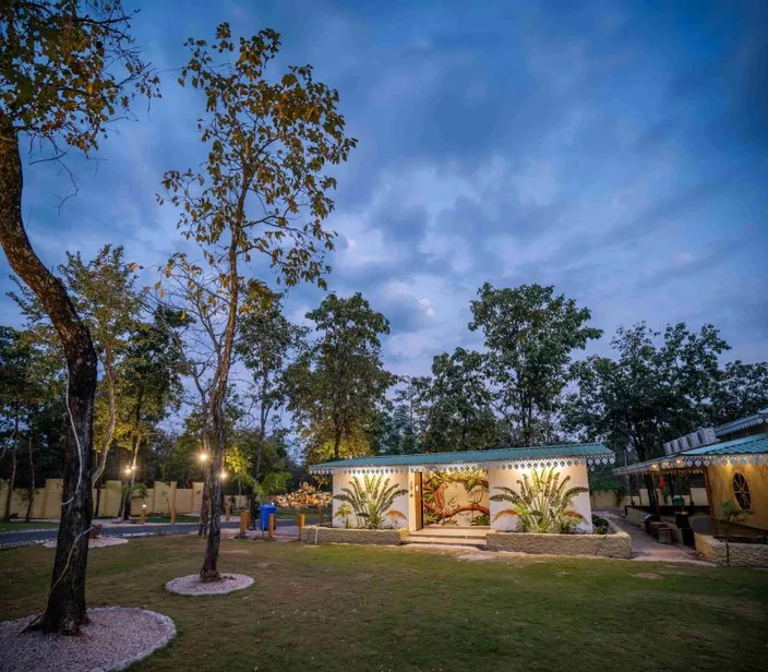 Cottages lit up at dusk under a blue sky at Palash Jungle Resort