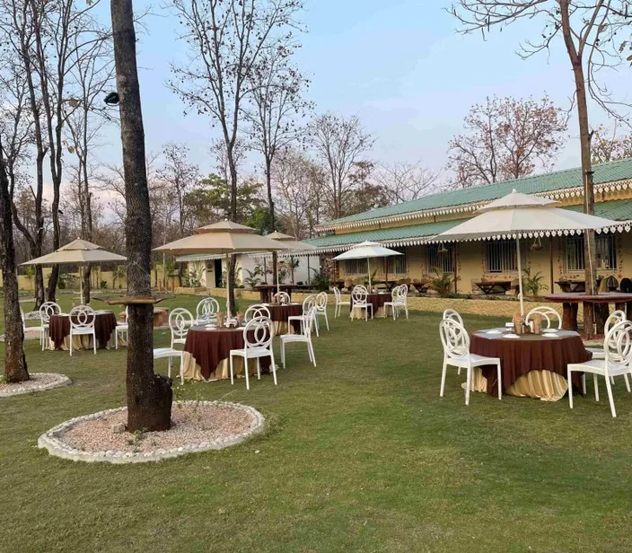 Garden dining tables with umbrellas on the lawn at Palash Jungle Resort